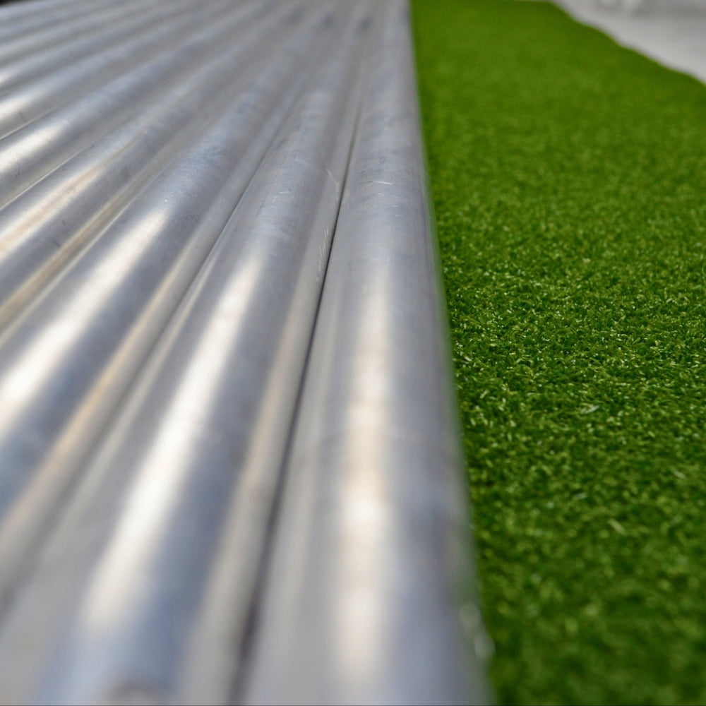 Close-up of metal pipes and green artificial grass on a white surface