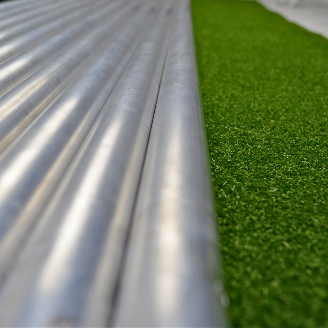 Close-up of metal pipes and green artificial grass on a white surface