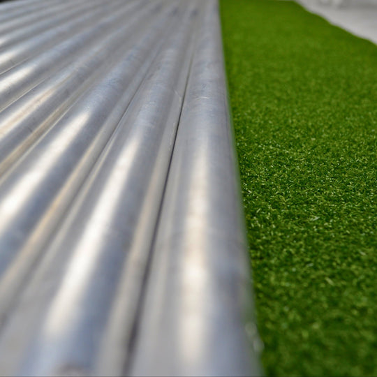Close-up of metal pipes and green artificial grass on a white surface
