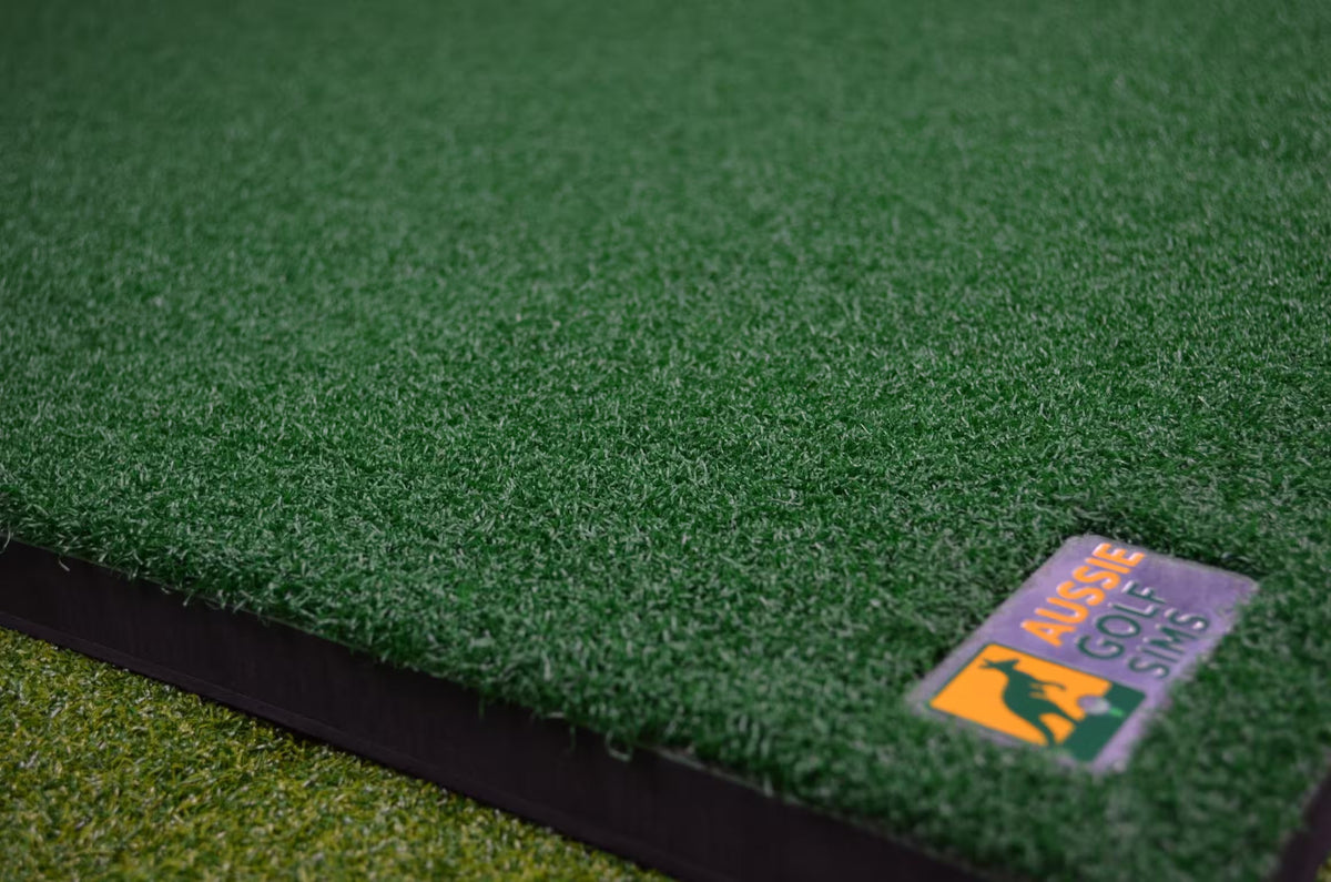 Close-up of green artificial turf or golf grass mat with a small visible logo patch reading 'Aussie Golf Sims' on the lower right edge.