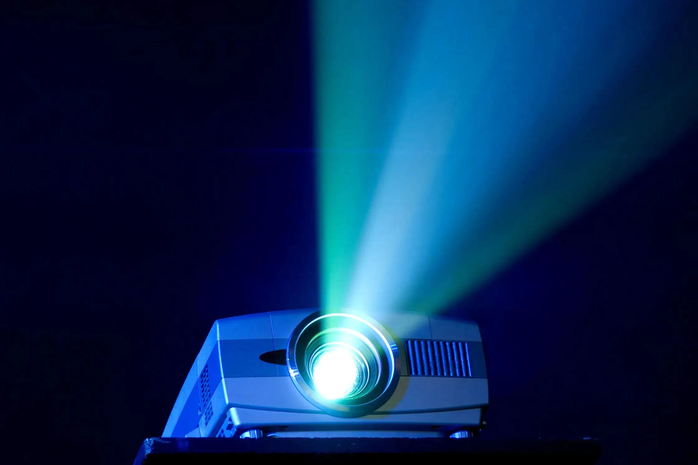 Modern silver projector casting vibrant blue and green light beams in a dark room.