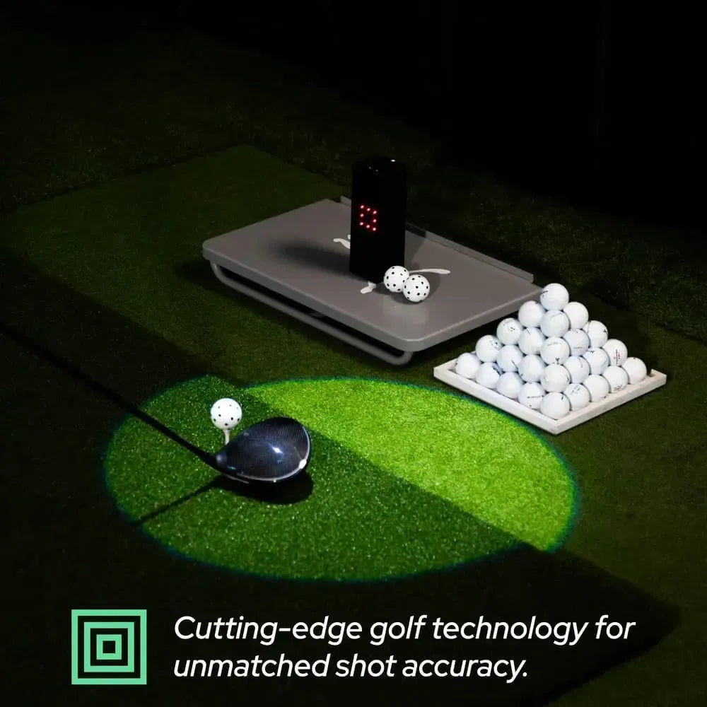 Black Square Golf home indoor launch monitor on a gray base, with golf balls and a driver on green turf.