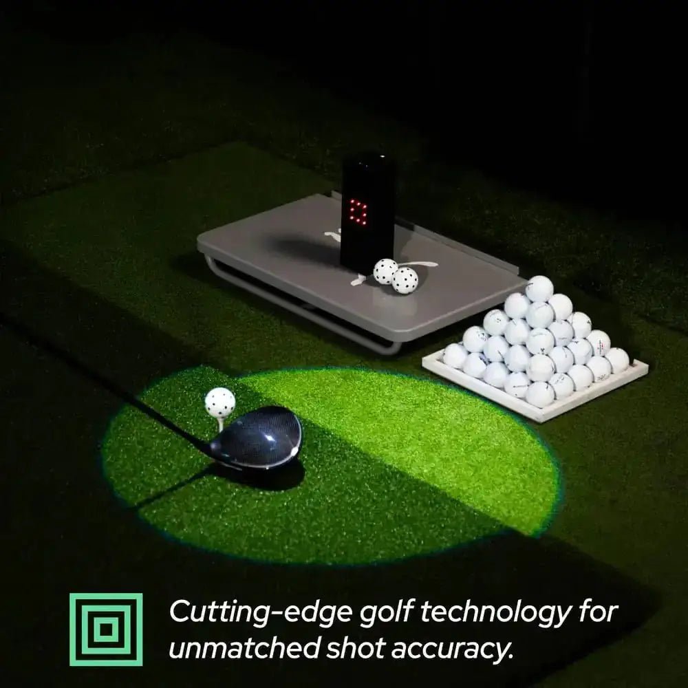 Black Square Golf home indoor launch monitor on a gray base, with golf balls and a driver on green turf.