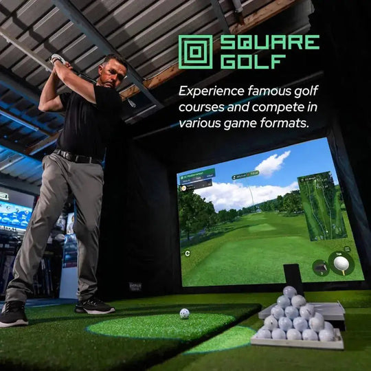Man swinging a golf club in an indoor simulator with a projected course, golf balls, and artificial turf.