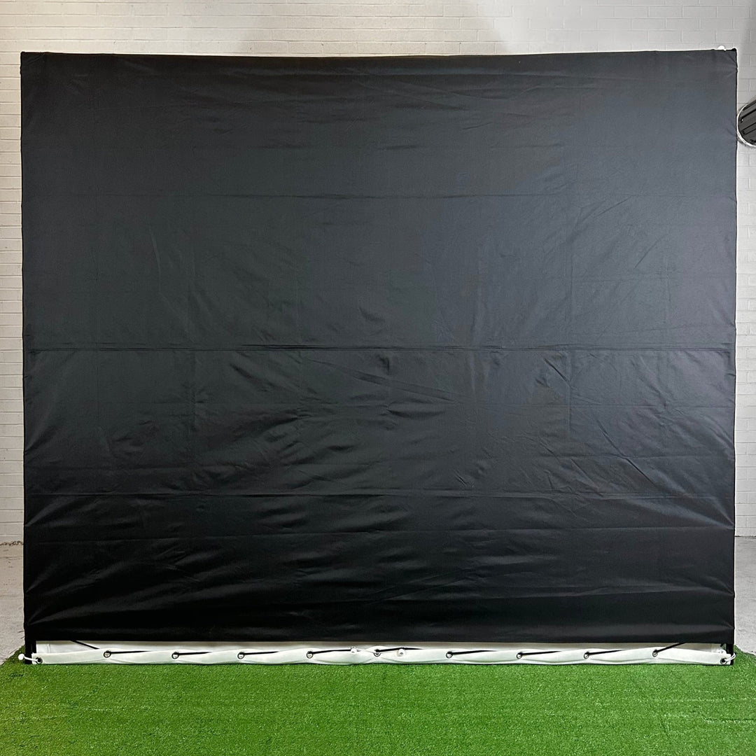 Black backing of golf simulator enclosure standing upright in white walled garage.