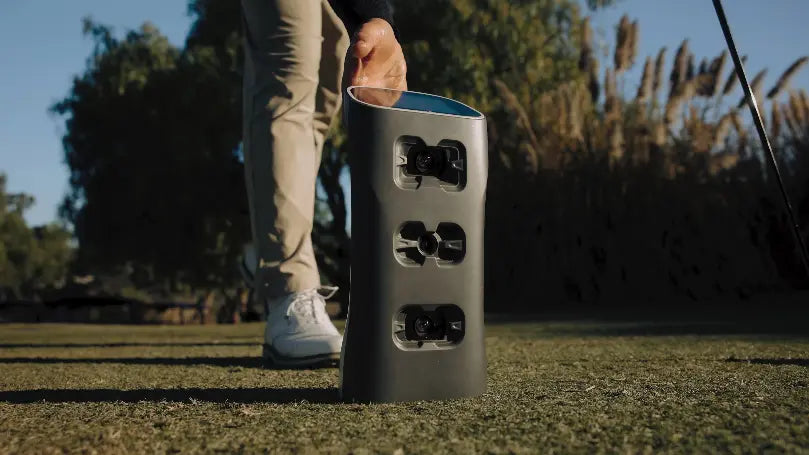 Person stepping on a golf ball with a GolfJoy Spica 3 launch monitor on a golf course
