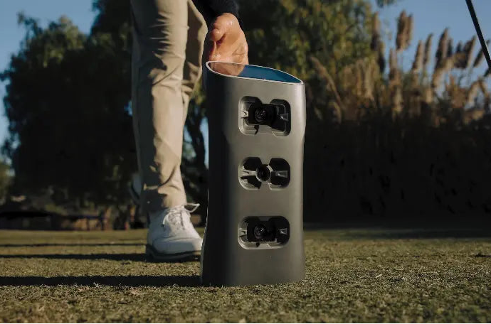Person stepping on a golf ball with a GolfJoy Spica 3 launch monitor on a golf course