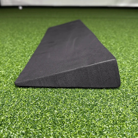 Dark gray EVA foam wedge for golf simulator screen protection, angled on green artificial turf.