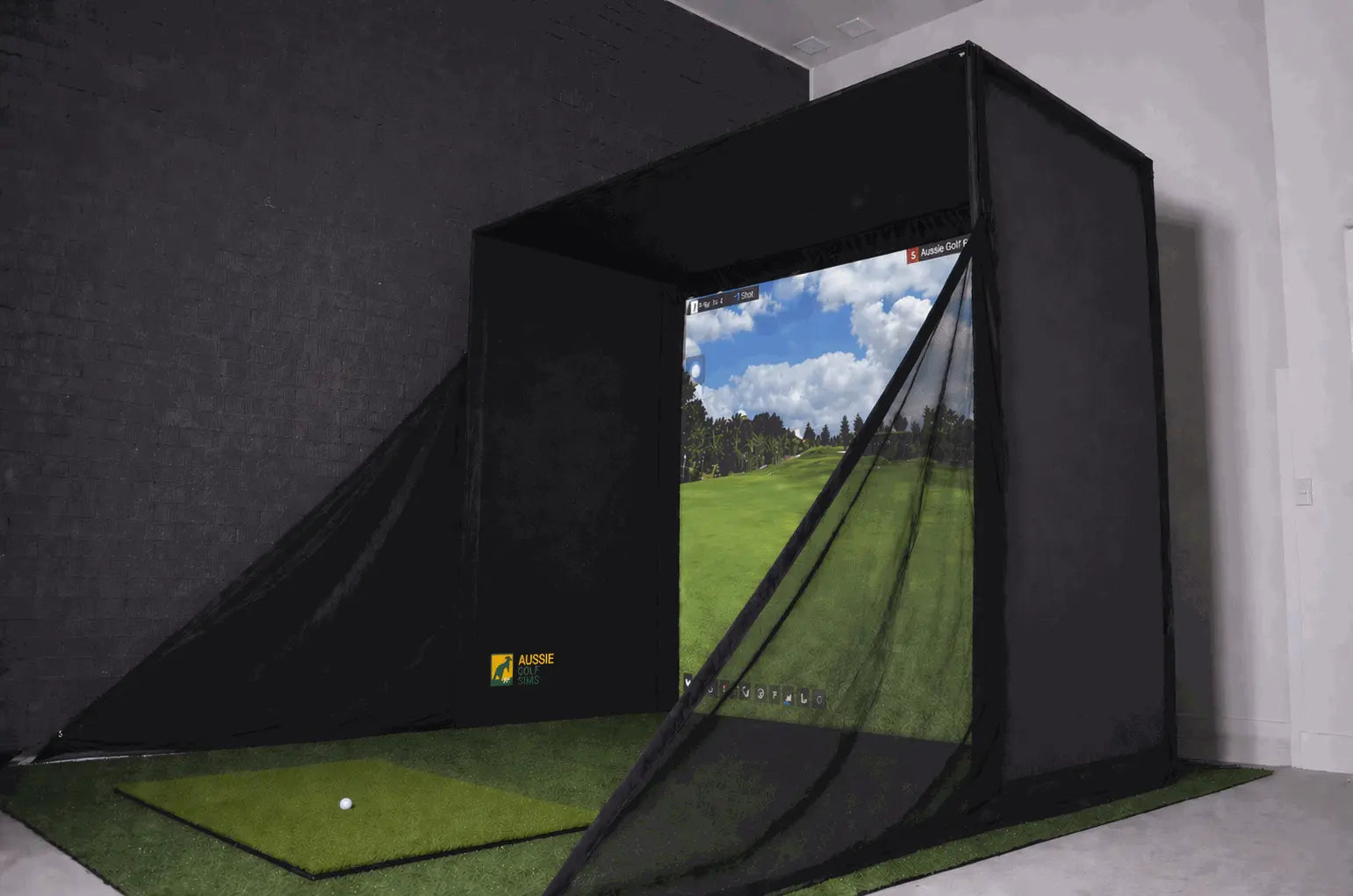 Golf simulator with screen displaying a golf course, surrounded by dark curtains.