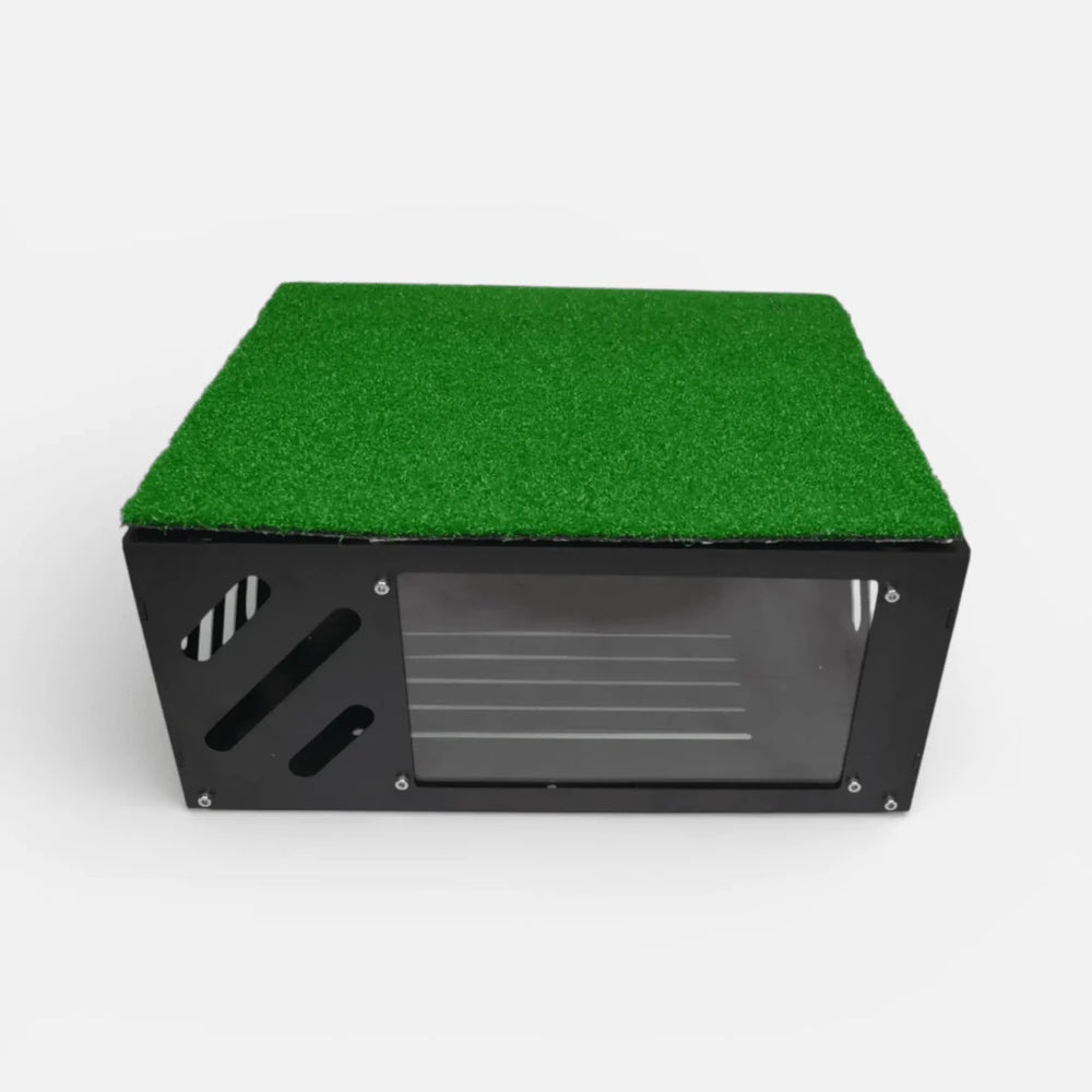 Black metal floor-mounted projector cover with green turf layer on top and clear front shield for golf simulator