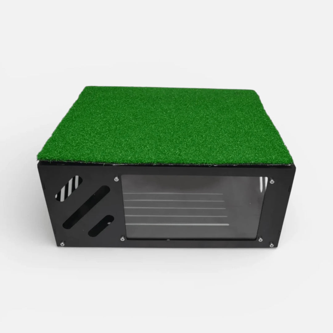 Black metal floor-mounted projector cover with green turf layer on top and clear front shield for golf simulator