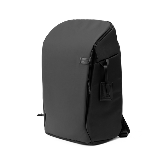 Sleek black backpack with a minimalist design, featuring a subtle logo patch and a hanging luggage tag.