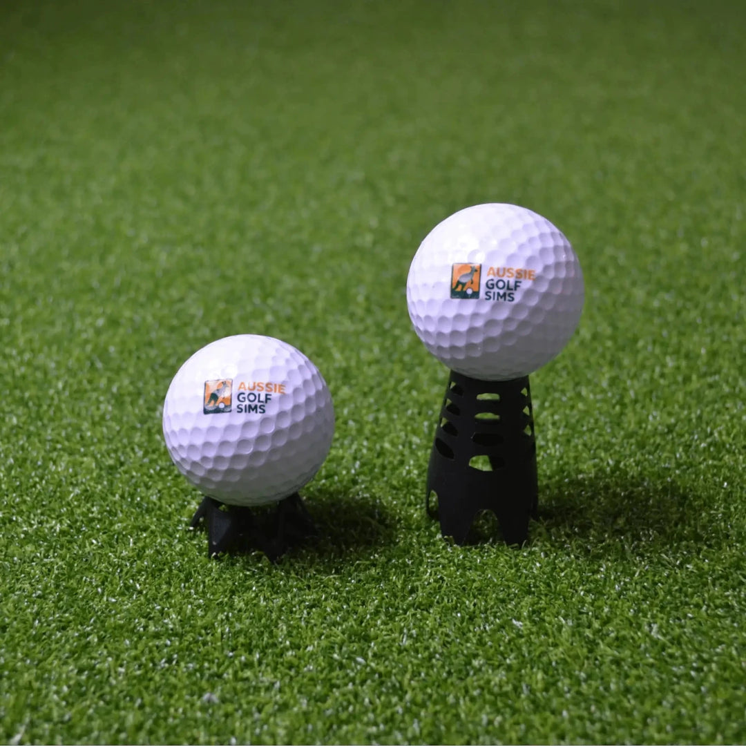 Side by side comparison of short and tall, black indoor golf tees sitting on green golf simulator turf with "Aussie Golf Sims" branded balls set up on them