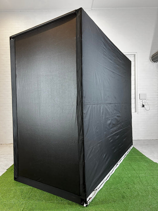 Side back angle of golf simulator enclosure in room with white wallson artificial grass
