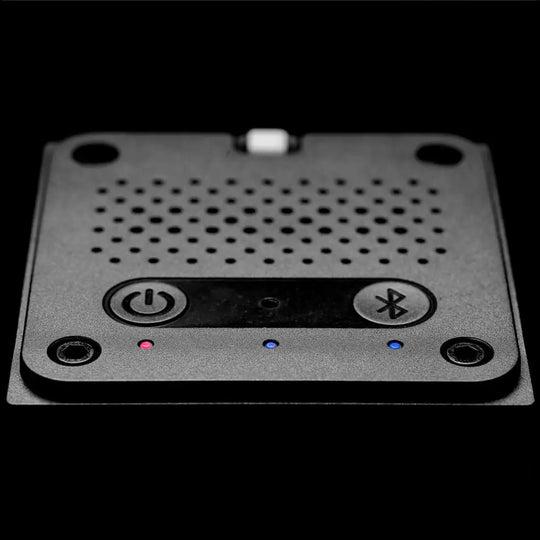 Compact black square golf launch monitor with power and Bluetooth buttons, perforated top, and indicator lights.
